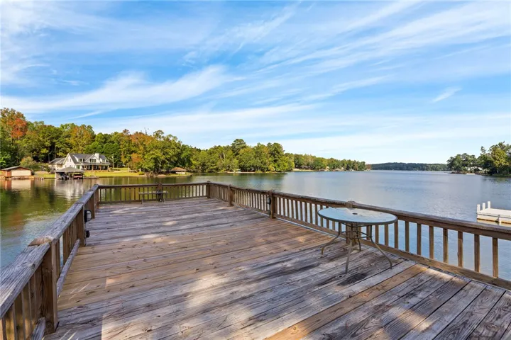 An expansive wooden dock extends over tranquil water, framed by lush trees and blue skies.