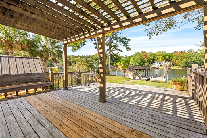 An overhead wooden pergola shades a spacious deck overlooking calm lake waters and private docks.