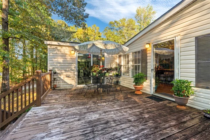Mature trees frame a spacious wooden deck attached to a light-sided home.