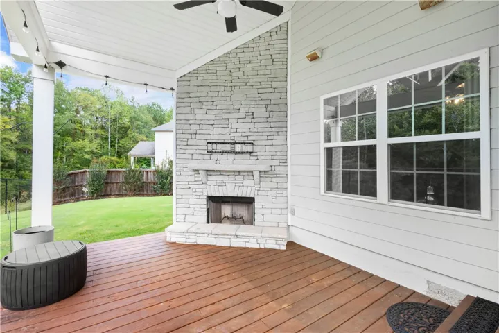 An inviting covered deck features a floor-to-ceiling stone fireplace overlooking the grassy backyard.