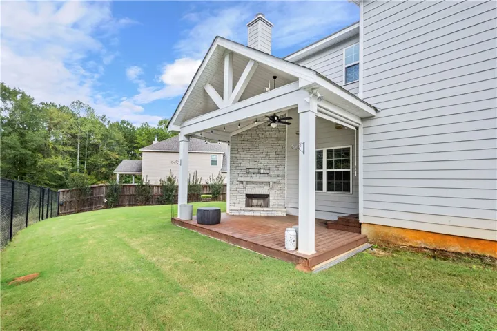 A spacious covered deck features a prominent stone fireplace overlooking the fenced grassy backyard.