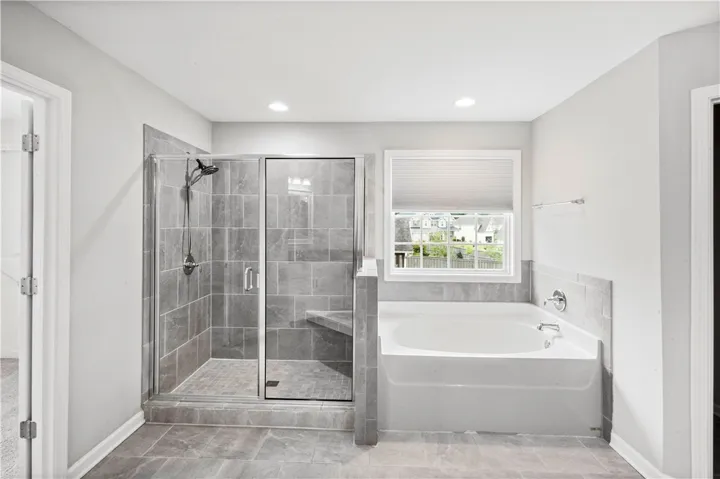 A spacious soaking tub sits adjacent to a glass-enclosed walk-in shower with stone tile surrounds.