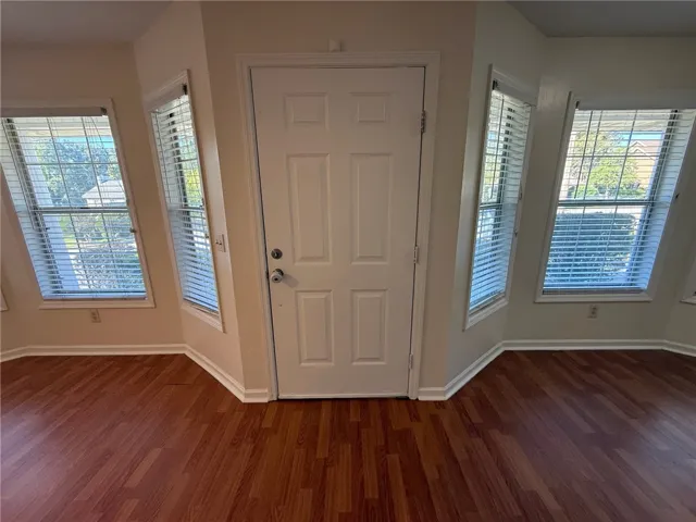 Rich wood flooring pairs with multiple windows flanking the central entry door.