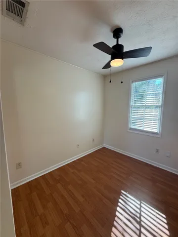 Rich wood flooring anchors this inviting bedroom illuminated by natural light through a classic window.
