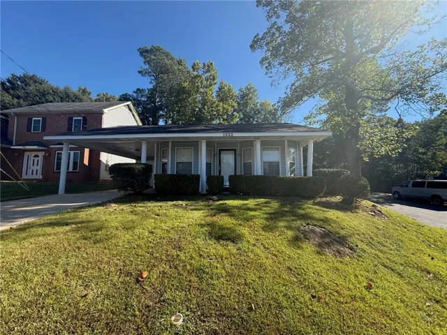 Mature trees shade the grassy front yard of this classic single-story home with a carport.
