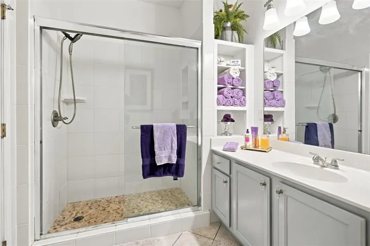A tiled walk-in shower features a sliding glass door alongside a vanity with built-in shelving.