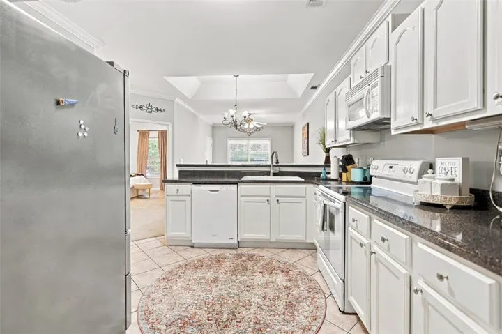 White cabinetry and dark countertops anchor this functional kitchen layout over tile flooring.