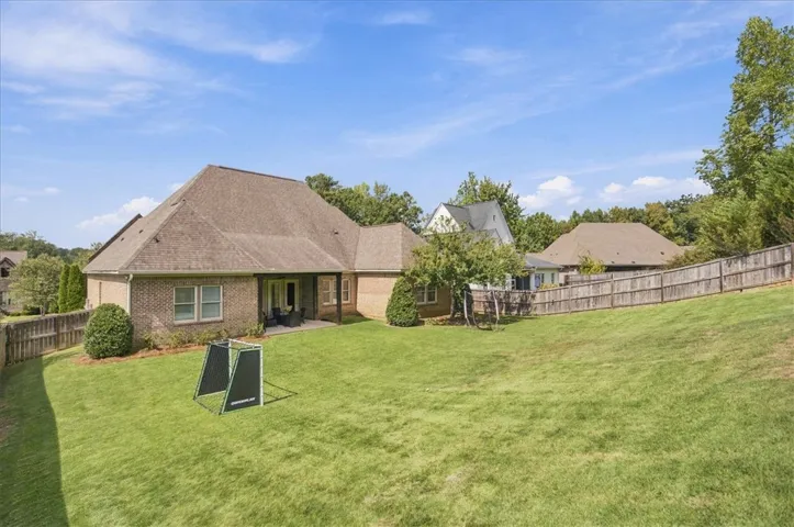 An expansive grassy backyard slopes gently upward toward a classic wood perimeter fence.