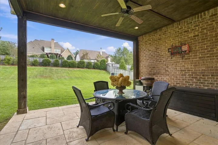 An inviting covered patio features a stone tile floor, brick accents, and views over the lawn.