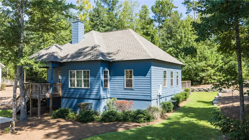 Mature trees frame a charming wood-sided exterior with a raised deck and manicured lawn.