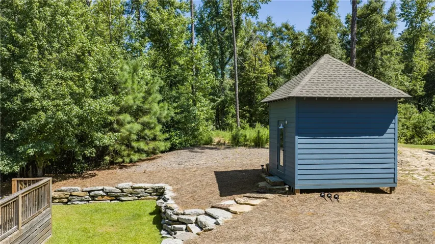 A detached storage shed stands bordered by a stacked stone retaining wall and mature trees.
