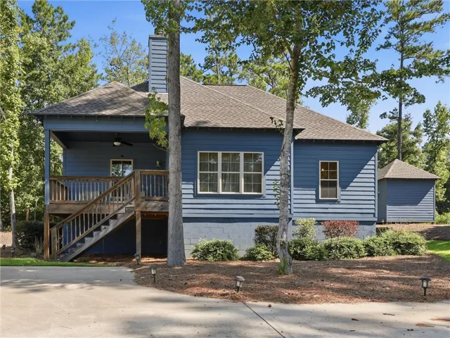 A wooden staircase leads to the covered porch of this wood-sided home surrounded by mature trees.