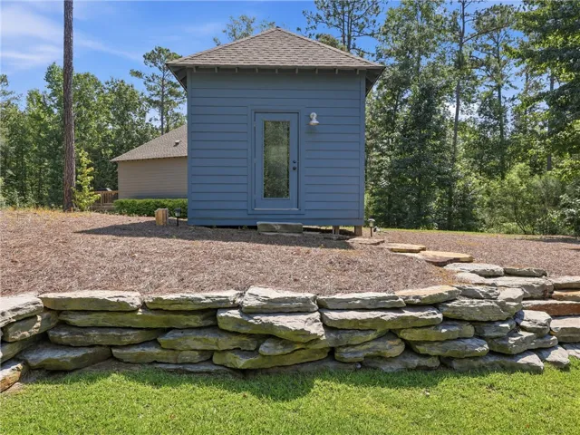 A detached storage building stands beyond a natural stone retaining wall in the grassy yard.