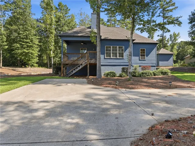 Mature trees frame a concrete driveway leading to a elevated back deck and storage shed.