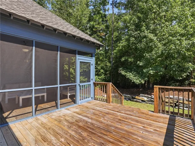 A spacious wooden deck adjoins a screened porch overlooking a wooded backyard landscape.