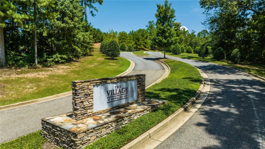 Stone masonry signage welcomes residents along a winding paved entry road bordered by mature trees.