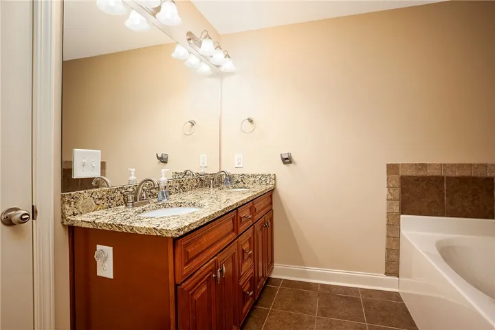 A spacious double vanity with granite counters stands adjacent to a deep soaking tub.