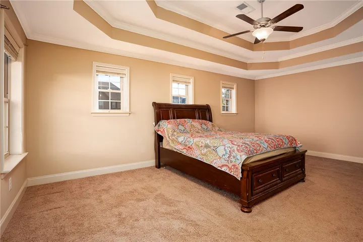 Plush carpeting anchors this spacious bedroom featuring a multi-tiered tray ceiling with crown molding.