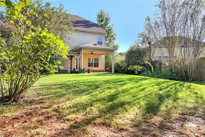 A spacious grassy lawn rolls toward a covered back porch and a wood-fenced border.