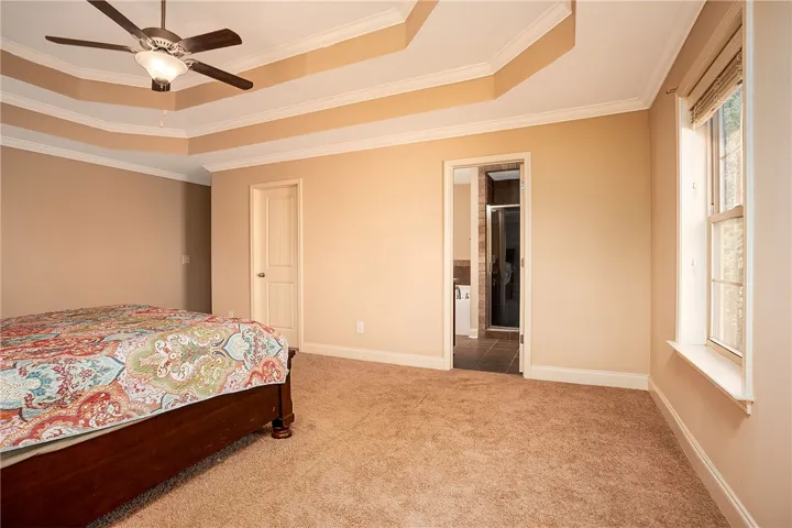 Plush carpeting and an elegant tray ceiling define this comfortable primary bedroom suite.