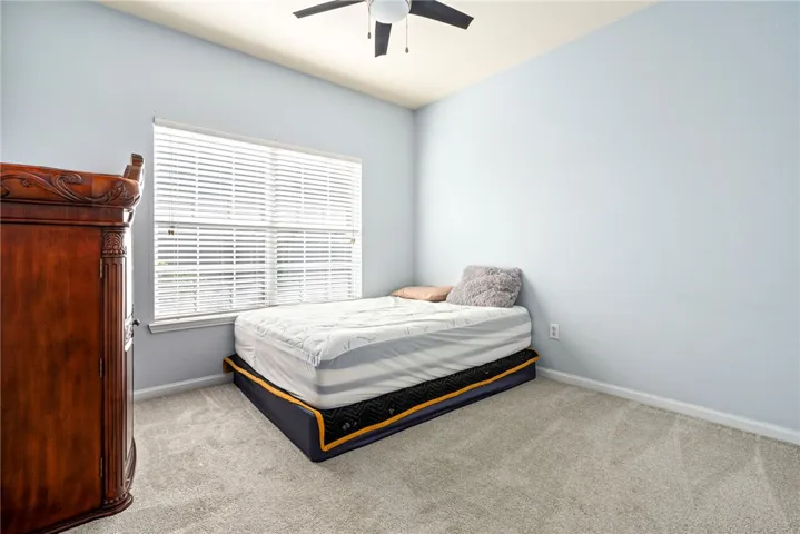 A wide window illuminates this bedroom featuring plush carpeting and neutral walls.