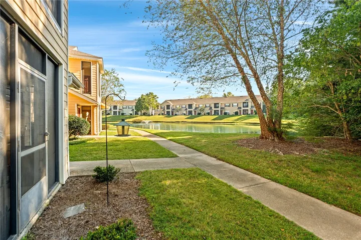 Paved pathways wind past grassy lawns toward a scenic neighborhood pond under clear blue skies.