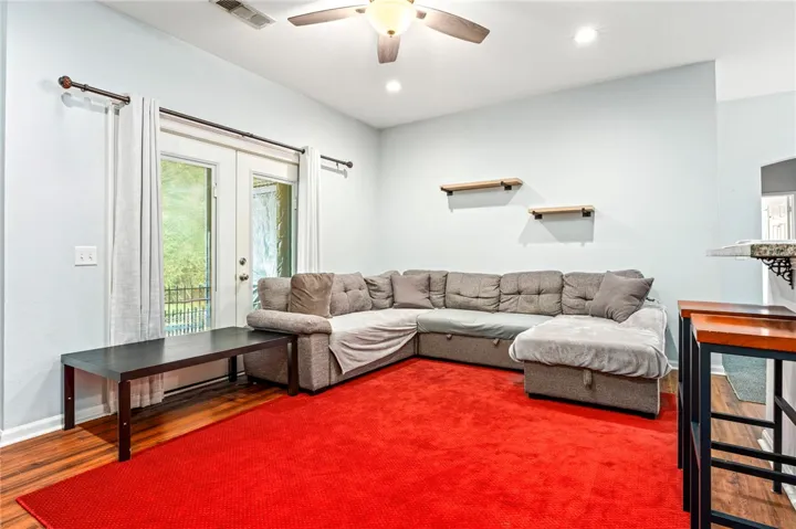 Glass doors open to the outdoors, illuminating the warm hardwood flooring and high ceilings.