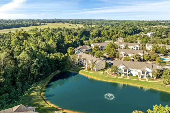 Mature trees frame a quiet neighborhood pond under wide open skies.