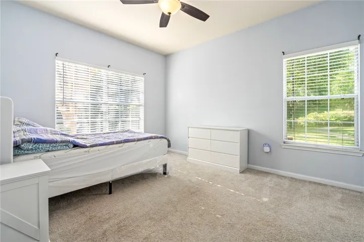 Plentiful natural light streams through multiple windows across the soft neutral carpeting.