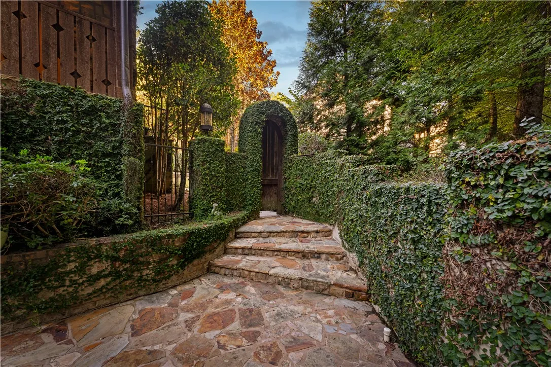 Lush ivy-covered stone walls frame a rustic flagstone pathway leading to an arched wooden gate.