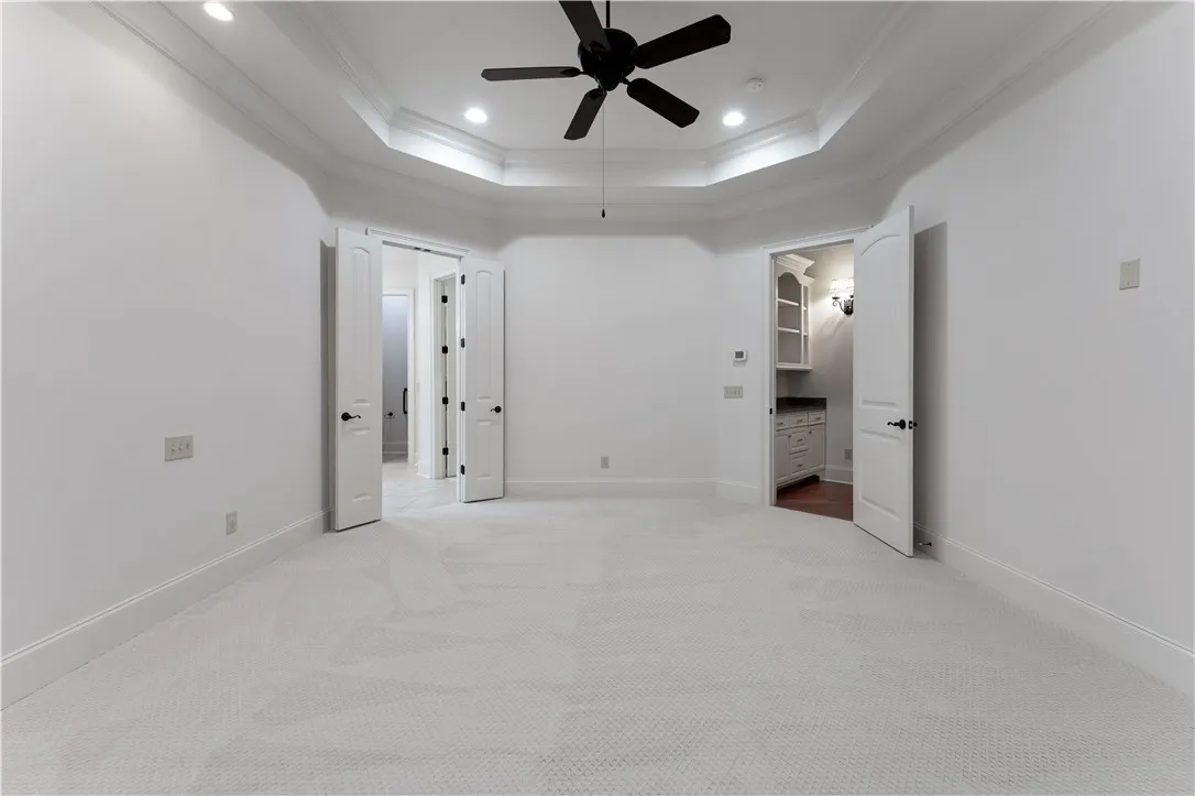 Plush carpeting anchors this spacious bedroom featuring an elegant tray ceiling and classic crown molding.