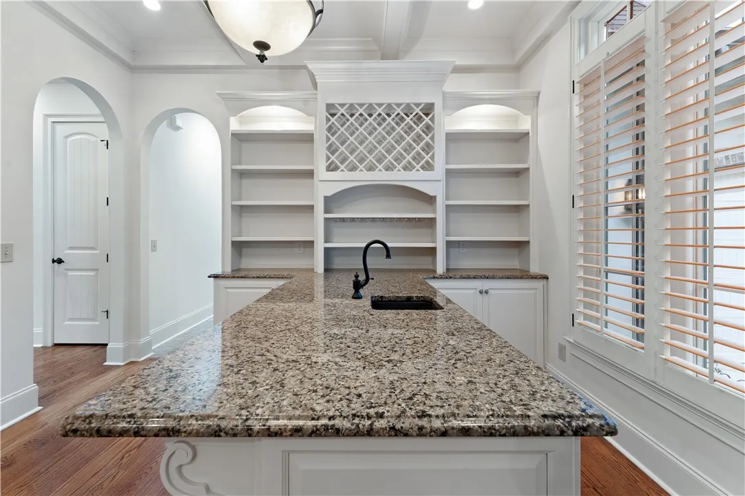 Polished granite countertops anchor this elegant butler pantry featuring built-in cabinetry and warm wood flooring.