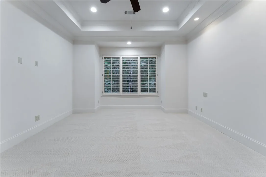 An elegant tray ceiling with crown molding highlights this carpeted bedroom.