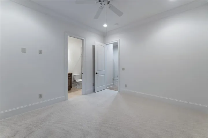 Plush carpeting and classic crown molding define this serene bedroom space with adjacent bath access.