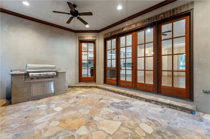 An outdoor kitchen integrates seamlessly with a covered stone patio featuring elegant glass doors.