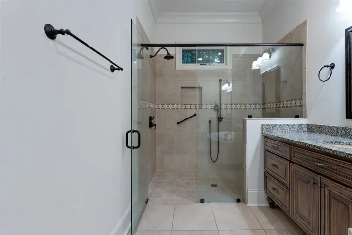 A spacious walk-in tile shower stands alongside a stone-topped vanity under elegant crown molding.