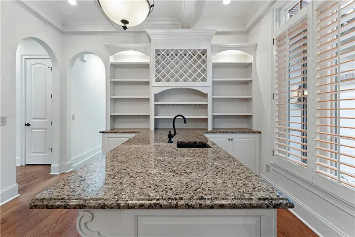 Polished granite countertops anchor this elegant butler pantry featuring built-in cabinetry and warm wood flooring.