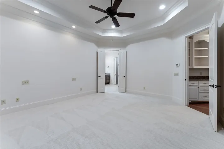 Plush carpeting anchors this spacious bedroom featuring a classic tray ceiling and recessed lighting.