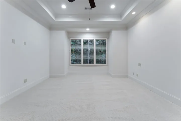 An elegant tray ceiling with crown molding highlights this carpeted bedroom.