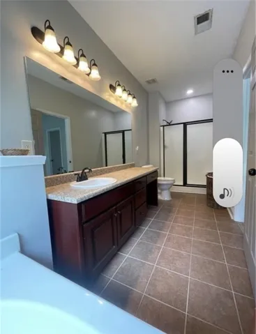 Tiled flooring and stone counters anchor this long bathroom design with a glass shower enclosure.