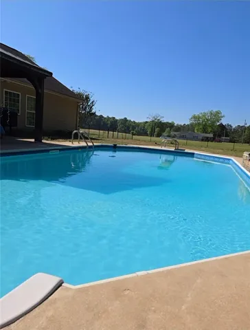 A spacious concrete pool deck overlooks a quiet pastoral setting under clear blue skies.