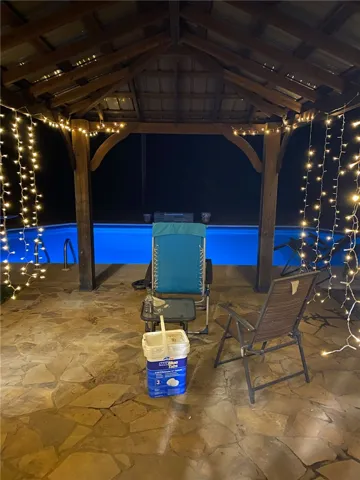 A stone patio shelter stands alongside the private swimming pool illuminated at night.