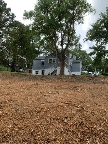 Mature trees frame a multi-level home featuring horizontal siding and exterior stair access.