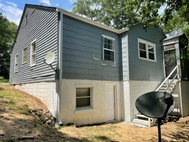 Sloped terrain borders a multi-level exterior showing wood siding and a walk-out block foundation.