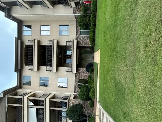 A well-maintained lawn stretches alongside this multi-story brick and stucco exterior with private balconies.