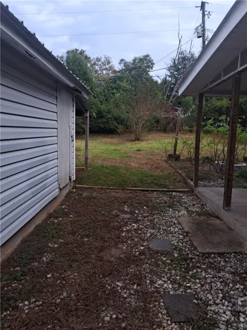 A spacious grassy lawn stretches behind the home, bordered by mature trees and outbuildings.