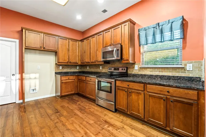 Rich wood cabinetry and stone countertops anchor this classic kitchen with warm wood flooring.