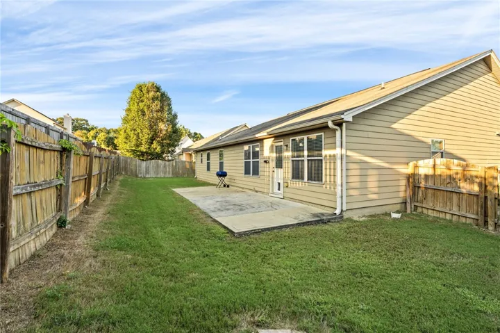 An inviting concrete patio overlooks a fully fenced grassy backyard under blue skies.