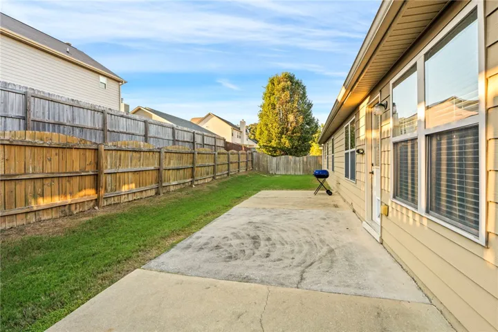 A spacious concrete patio overlooks the grassy backyard bordered by a sturdy privacy fence.