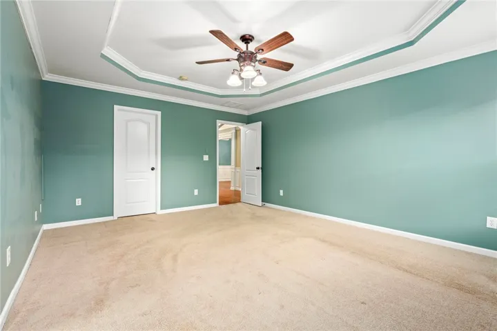 A tray ceiling highlighted by crown molding frames this comfortable bedroom featuring wall-to-wall carpet.